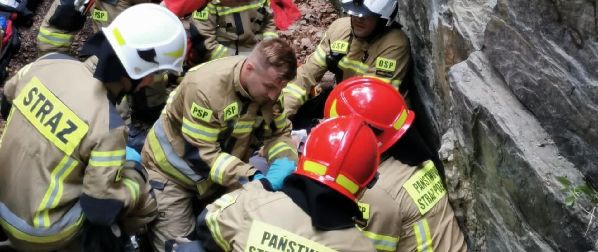 Zdjęcie przedstawia strażaków ubranych w mundury specjalne, udzielających pierwszej pomocy osobie poszkodowanej w Górach Opawskich.