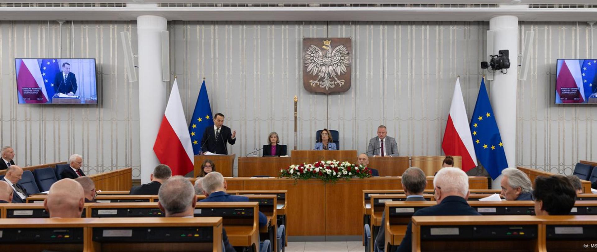 Sala posiedzeń z polskimi i unijnymi flagami oraz uczestnikami spotkania przy prezydium.