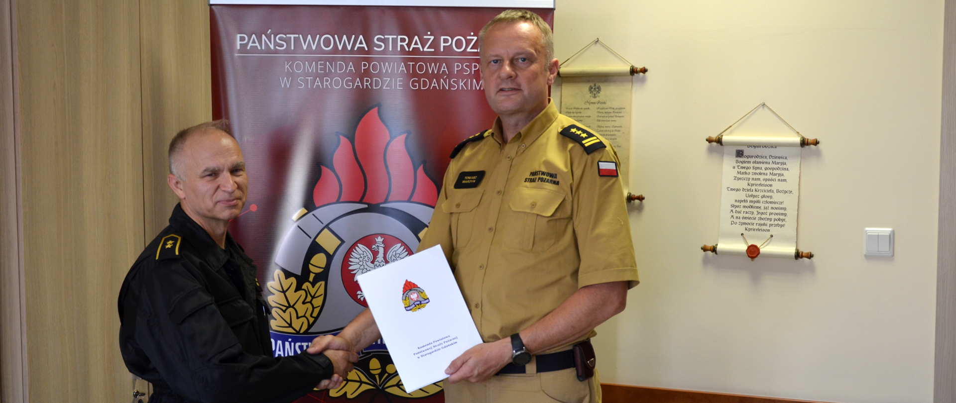 Na zdjęciu moment wręczenia dyplomu przez komendanta powiatowego, w tle baner PSP