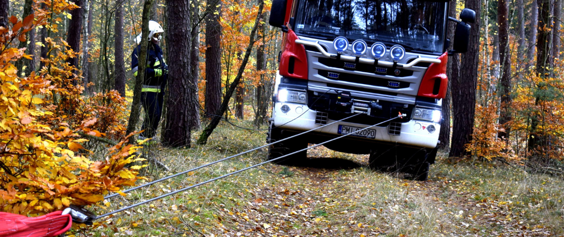 Na zdjęciu samochód pożarniczy, który wciągany jest przez wyciągarkę samochodową na drodze polnej w lesie.