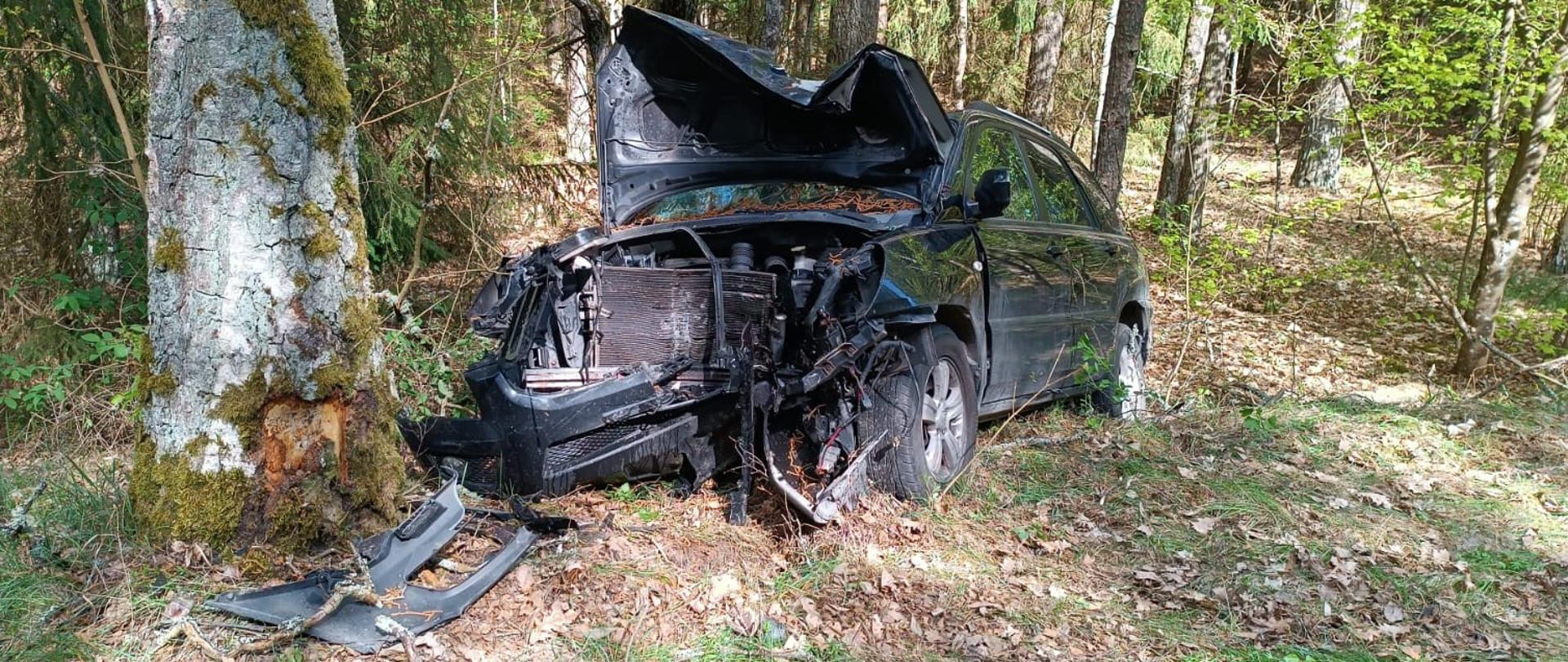 Zdjęcie przedstawia pojazd osobowy po zderzeniu z drzewem w miejscowości Skocze, gm. Gołdap na drodze powiatowej. Na obrazie widoczne są uszkodzenia przodu samochodu