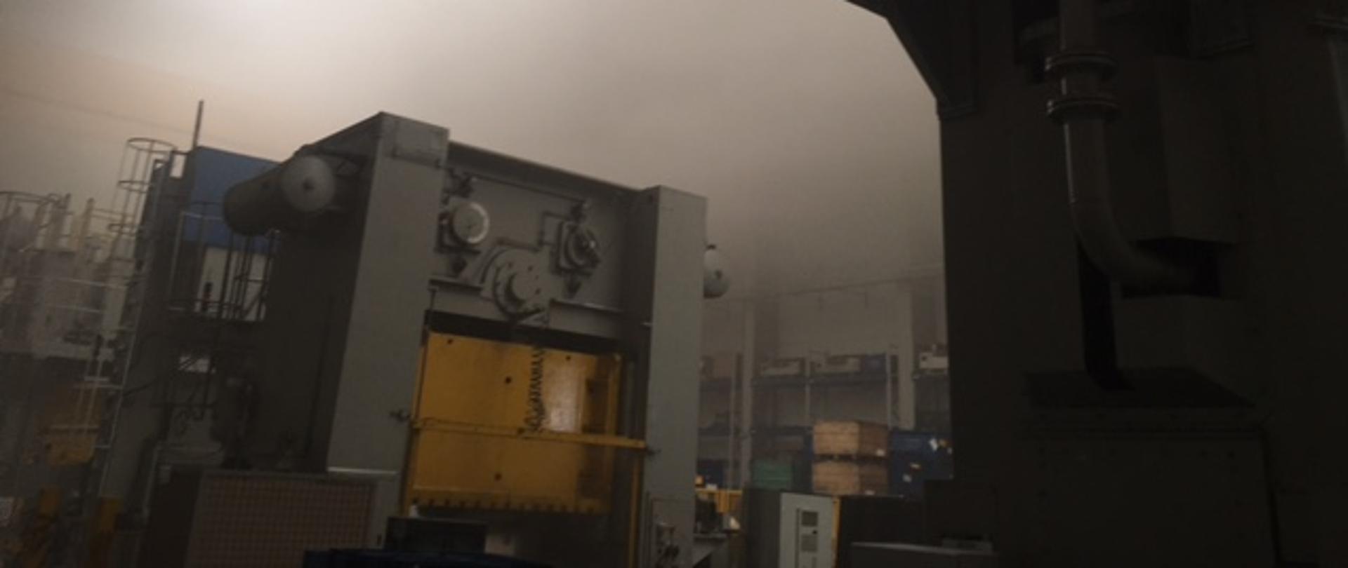Zadymione wnętrze hali produkcyjnej.