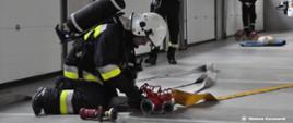 Strażak ćwiczy budowanie linii gaśniczej podczas egzaminu na strażaka ratownika OSP