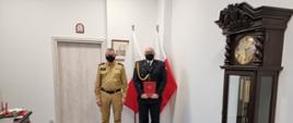 Pomorski komendant wojewódzki Państwowej Straży Pożarnej stoi wspólnie ze strażakiem trzymającym czerwoną teczkę.