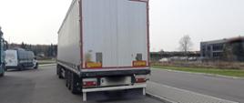 Na pierwszym planie: tył naczepy podpiętej do ciągnika siodłowego. Kontrolowany zespół pojazdów stoi w zatoce kontrolnej. W tle: oznakowany furgon mazowieckiej Inspekcji Transportu Drogowego stoi obok zestawu ciężarowego.