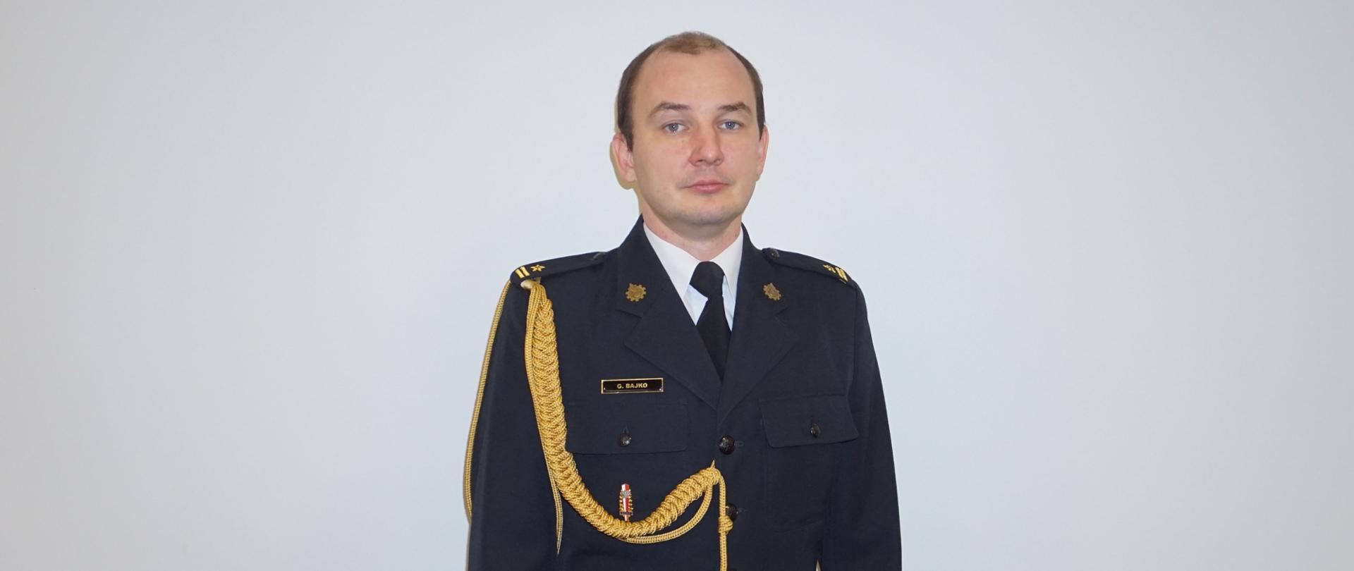 Zastępca Komendanta Powiatowego mł. bryg. Grzegorz Bajko w granatowym mundurze na białym tle.