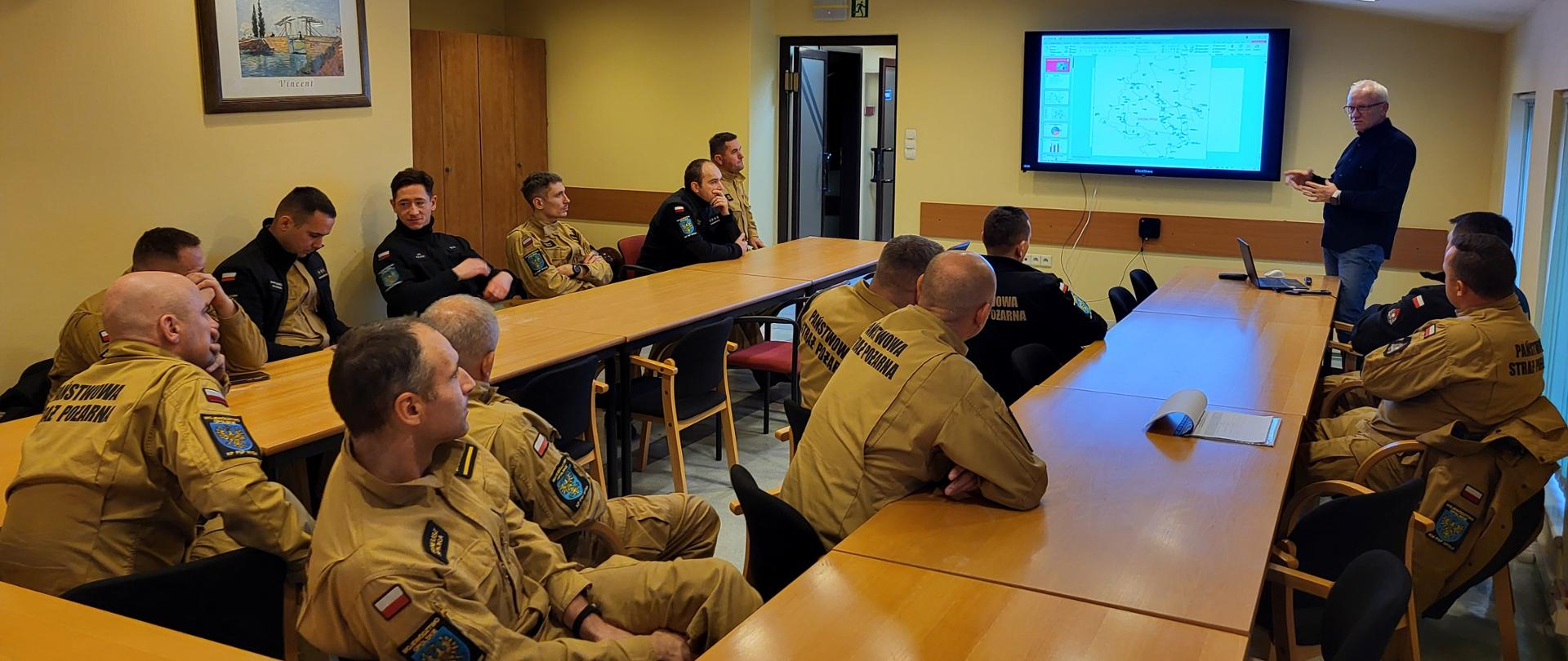 Uczestnicy warsztatów JRG w sali konferencyjnej słuchają prezentacji z mapą operacyjną na