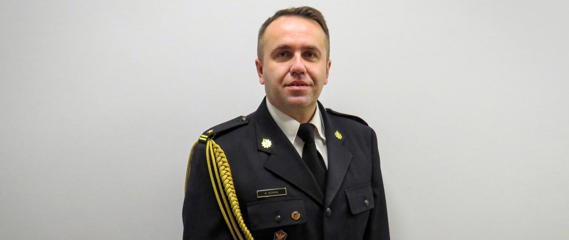 Na zdjęciu portretowym znajduje się zastępca komendanta powiatowego psp - młodszy brygadier Krystian Kowal, który jest ubrany w mundur galowy oraz białą koszulę.
