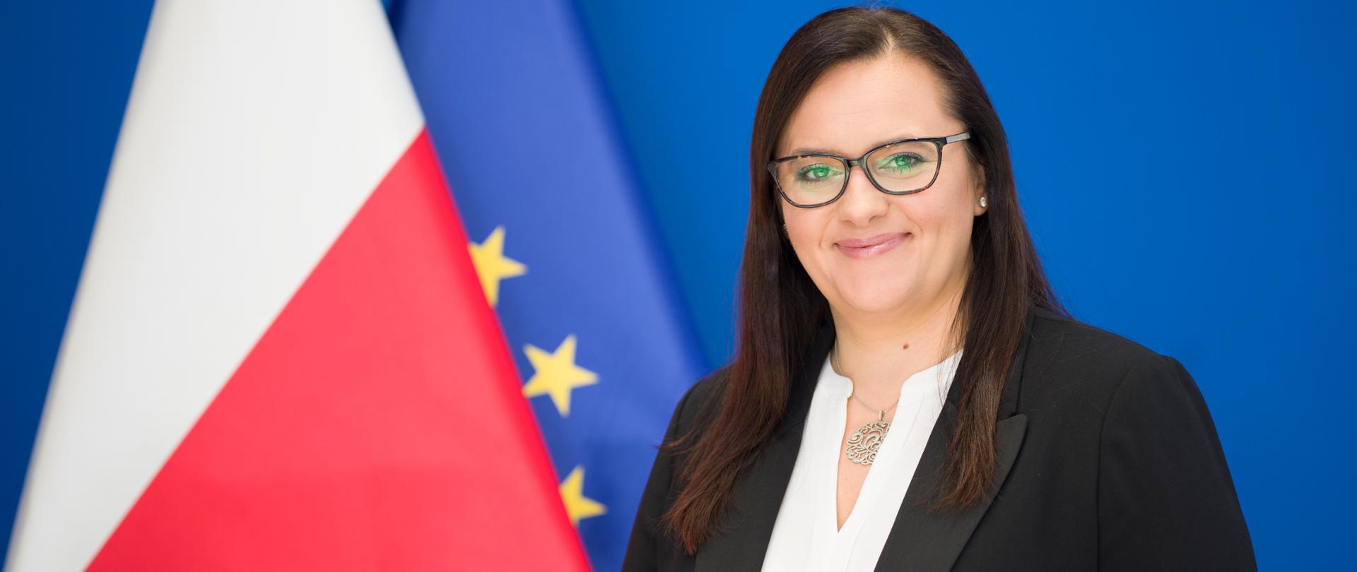 Na zdjęciu minister funduszy i polityki regionalnej Małgorzata Jarosińska-Jedynak stoi obok flag PL i UE