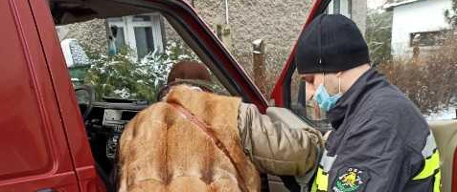 zdjęcie przedstawia strażaka który pomaga wsiąść starszej osobie do samochodu straży pożarnej.