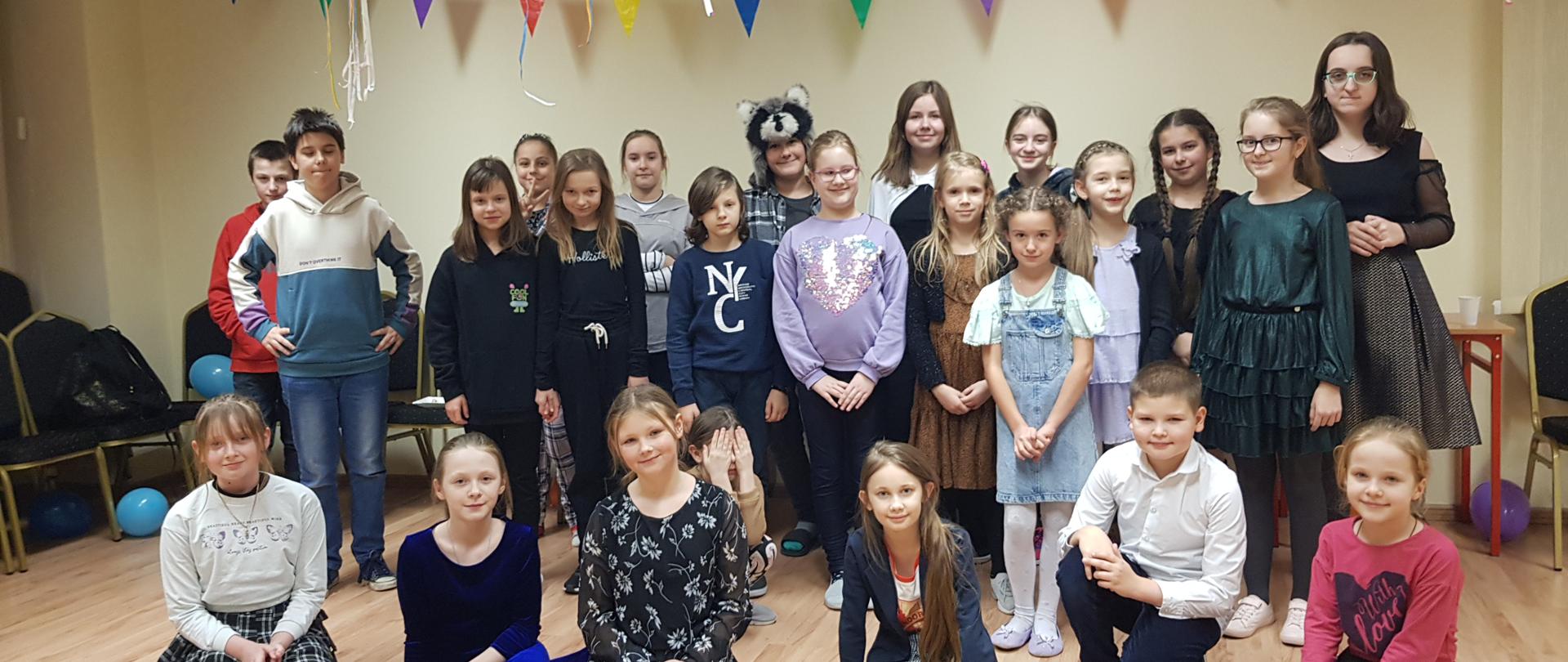 Dzieci ustawione w grupie do wspólnego zdjęcia. W tle widać girlandy, balony oraz serpentyny.