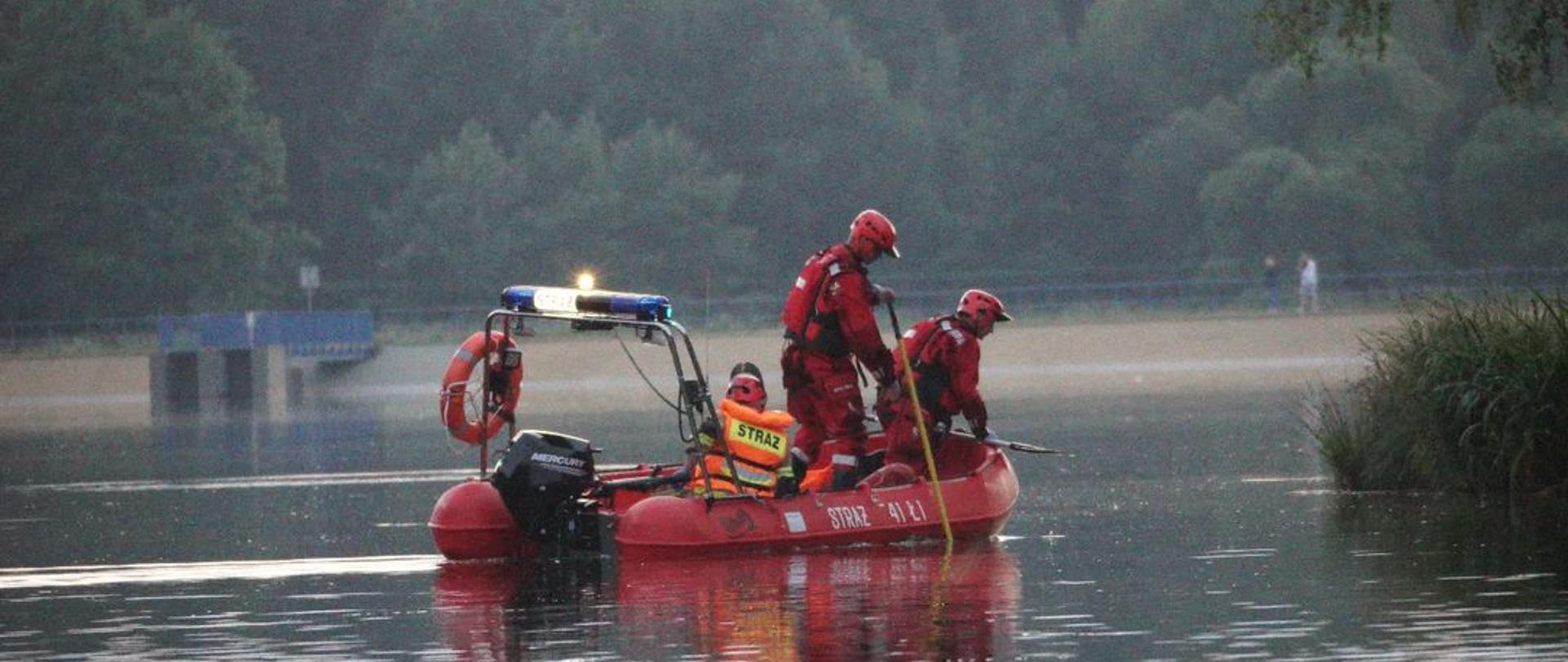 Strażacy w ubraniach specjalnych szukają osoby w wodzie przy użyciu łodzi.