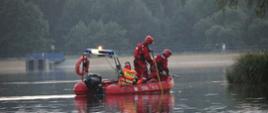 Strażacy w ubraniach specjalnych szukają osoby w wodzie przy użyciu łodzi.