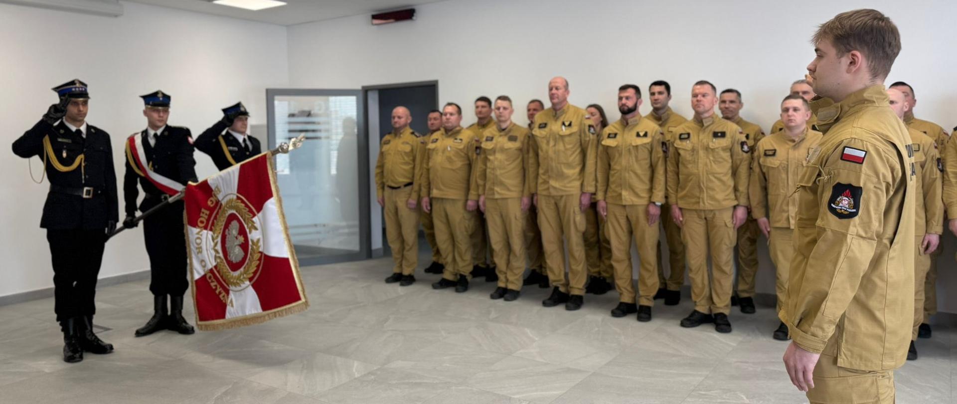 Uroczysty apel służbowy, podczas którego poczet sztandarowy Państwowej Straży Pożarnej prezentuje sztandar przed funkcjonariuszami stojącymi w szyku.