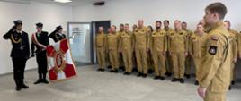 Uroczysty apel służbowy, podczas którego poczet sztandarowy Państwowej Straży Pożarnej prezentuje sztandar przed funkcjonariuszami stojącymi w szyku.