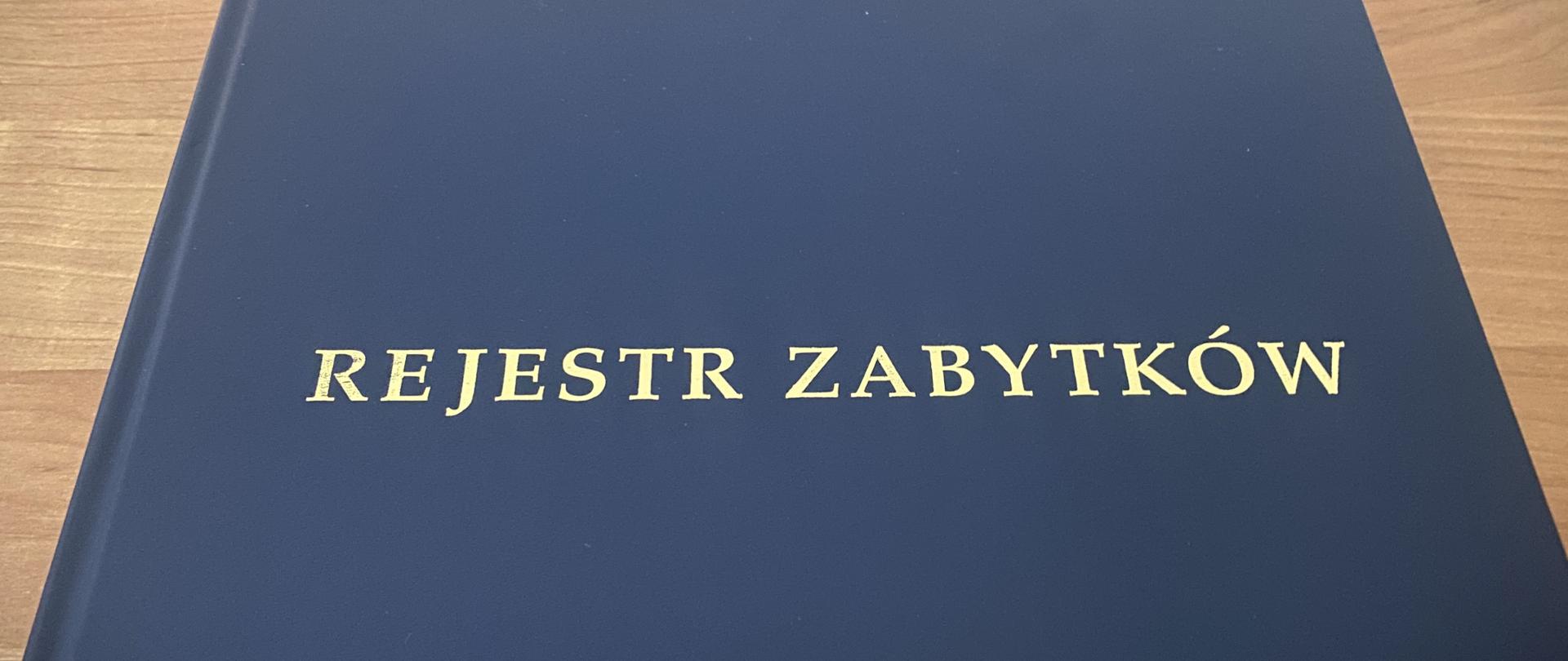 granatowa okładka księgi z dużym napisem złotymi literami "REJESTR ZABYTKÓW"