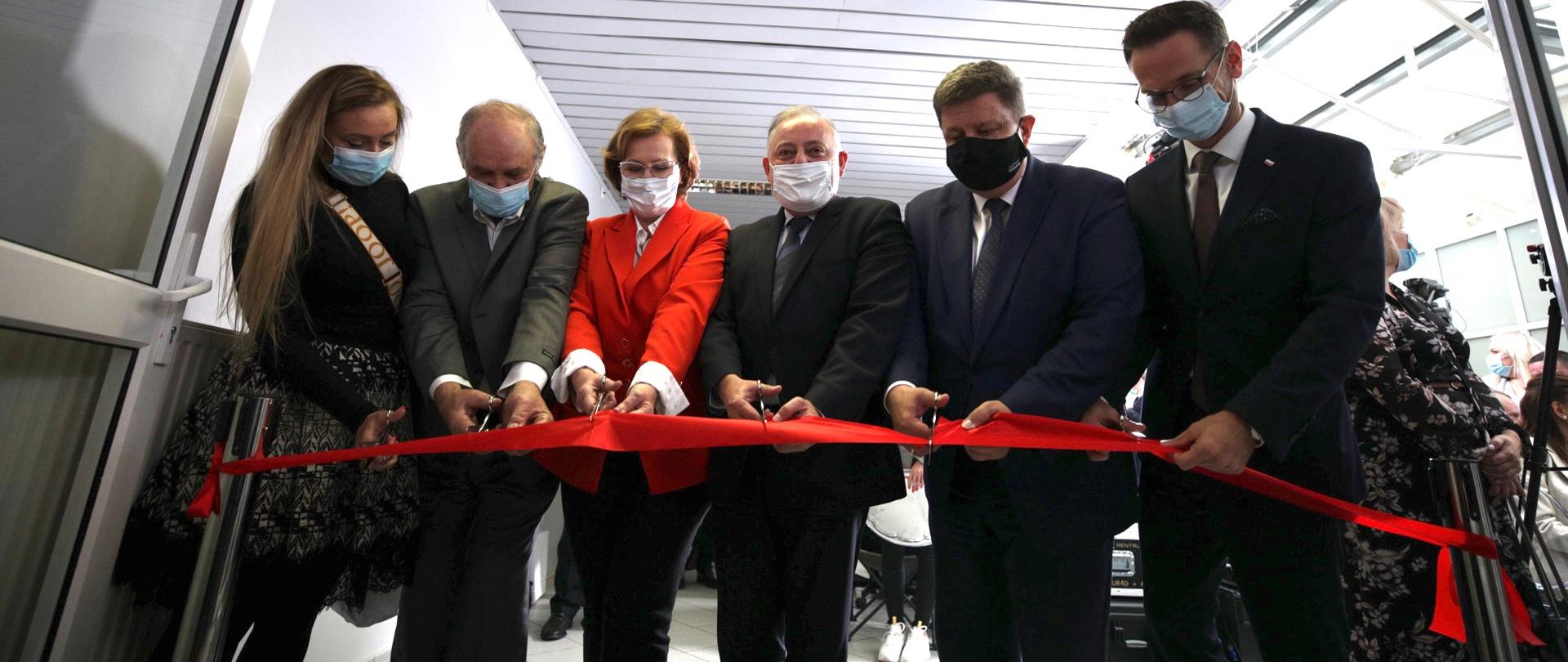 Sześć osób w pomieszczeniu przecina czerwoną wstęgę. Pierwszy od prawej Waldemar Buda.