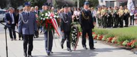 Na zdjęciu znajdują się delegacje z wiązankami kwiatów, w tle widać poczty sztandarowe oraz innych gości. Całość uroczystości odbywa się przed pomnikiem
