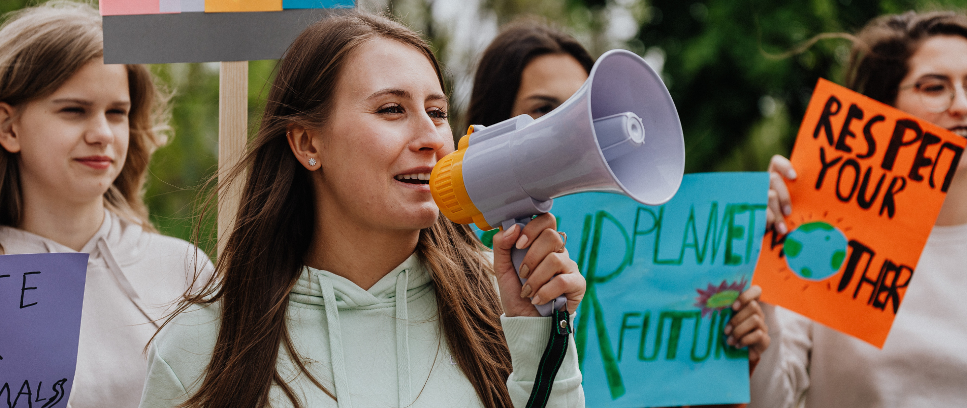 na zdjęciu widoczne są kobiety w trakcie protestu. W dłoniach trzymają transparenty z różnymi hasłami oraz megafon. 