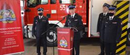 Zdjęcie przedstawia starszego brygadiera Zbigniewa Łyszkowicza Zastępcę Komendanta Wojewódzkiego Państwowej Straży Pożarnej w Łodzi stojącego przy mównicy, komendanta i zastępcę komendanta powiatowego państwowej straży pożarnej w wieluniu oraz strażaka prowadzącego uroczystość w mundurach wyjściowych, w tle samochód pożarniczy