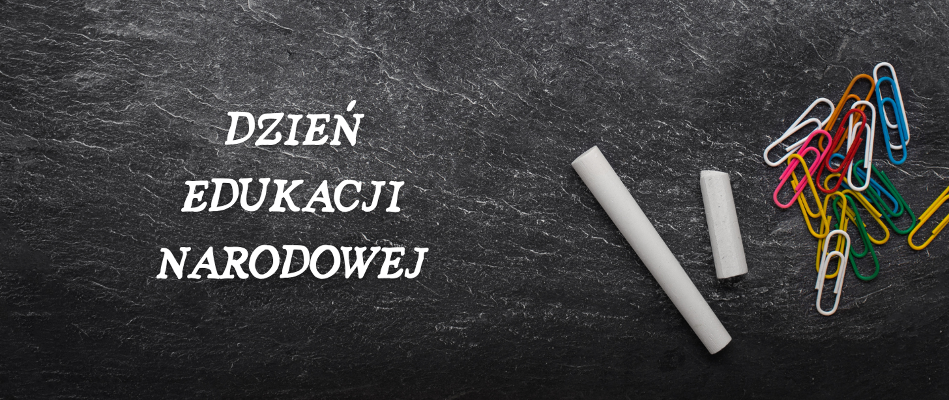 Tablica szkolna z napisem Dzień Edukacji Narodowej. Z boku widoczne dwa kawałki kredy oraz garść kolorowych spinaczy biurowych.