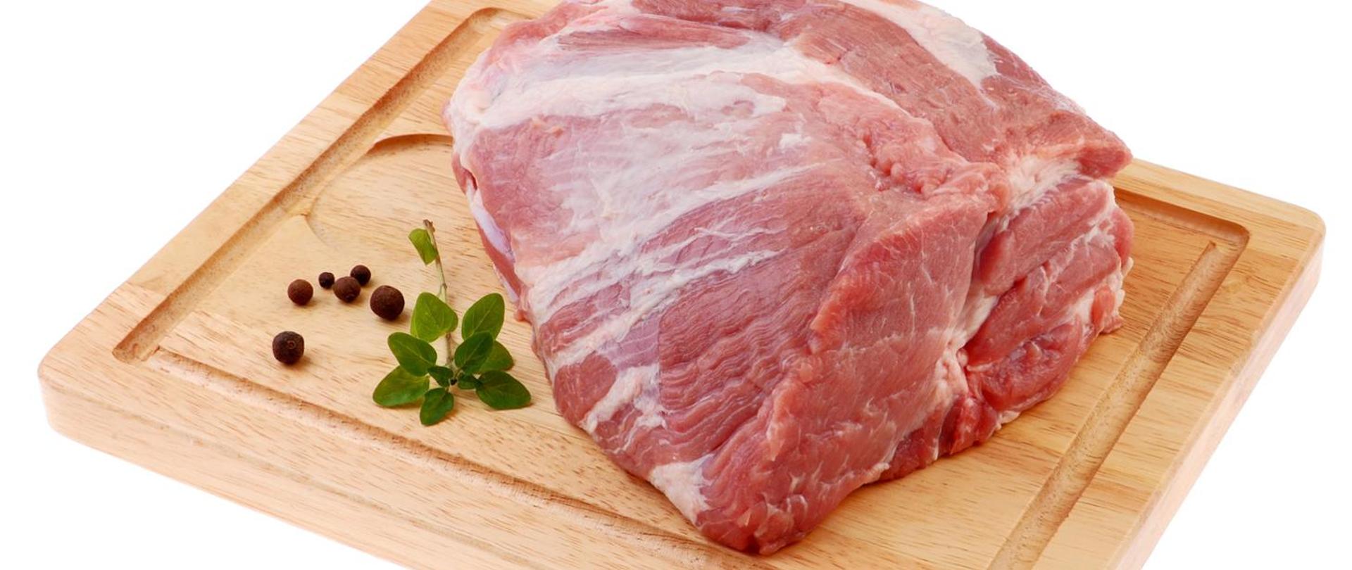 Grafika przedstawia kawałek surowego mięsa umieszczonego na drewnianej desce kuchennej.