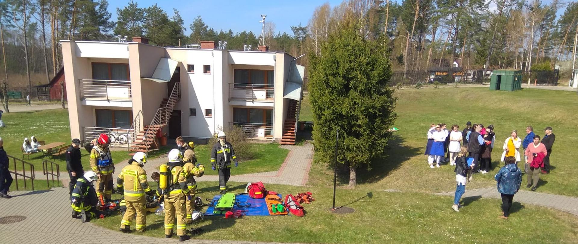 Strażacy oraz uczestniczy ćwiczeń zgromadzeni przed jednym z domów ośrodka.