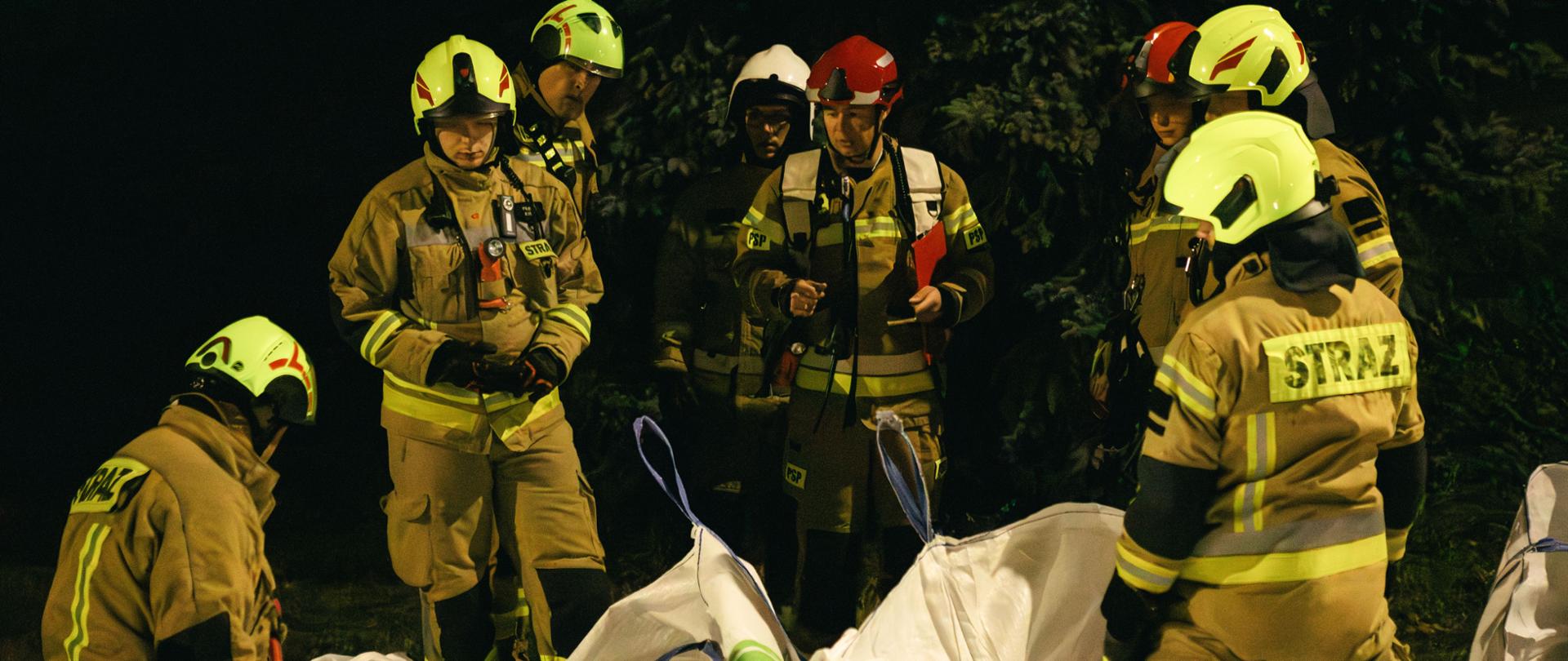 Strażacy przy workach z piaskiem w żółtych ubraniach specjalnych. 