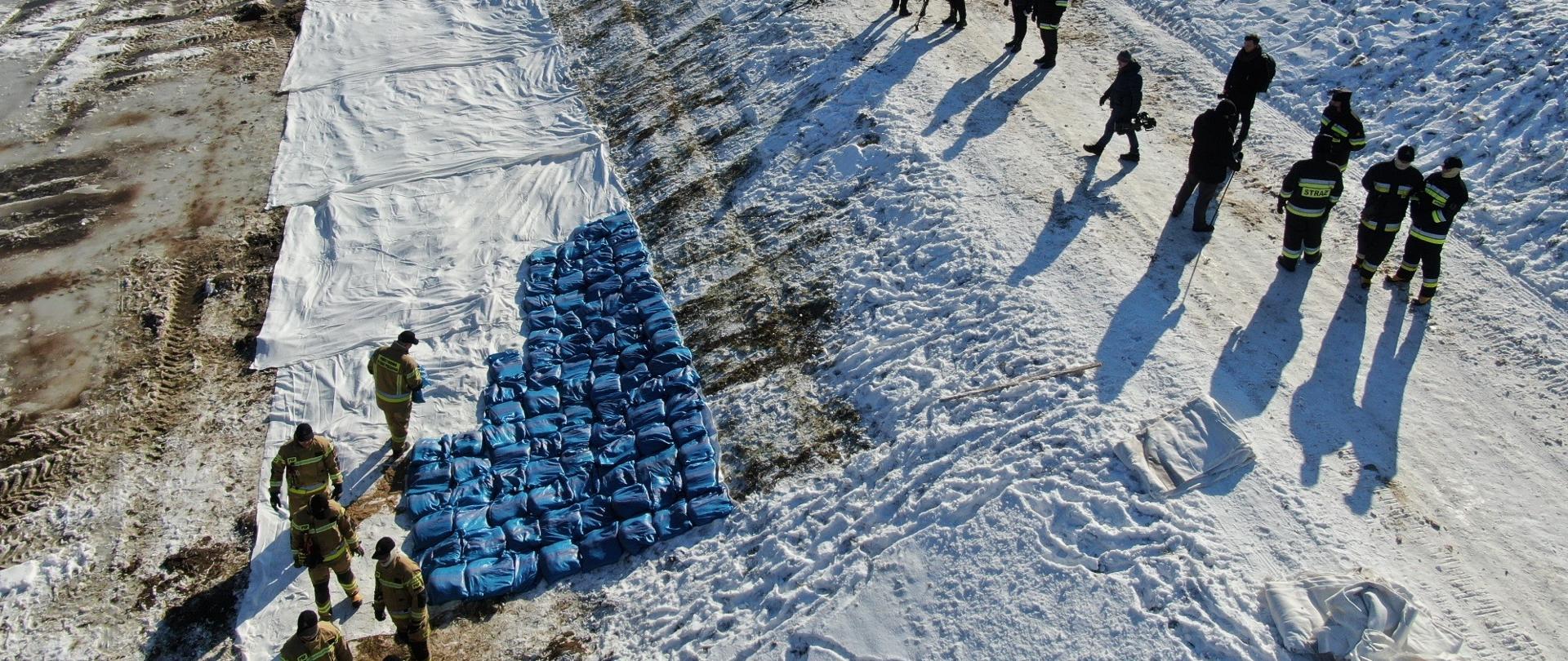 Strażacy podczas układania worków z piaskiem na wale przeciwpowodziowym. Ujęcie wykonane z góry.