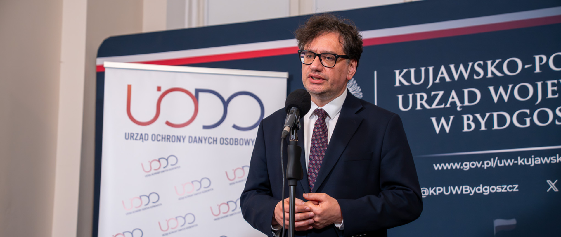 Prezes Urzędu Ochrony Danych Osobowych Mirosław Wróblewski przemawia podczas konferencji prasowej w Kujawsko-Pomorskim Urzędzie Wojewódzkim. W tle widać ściankę Kujawsko-Pomorskiego Urzędu Wojewódzkiego oraz rollup Urzędu Ochrony Danych Osobowych.