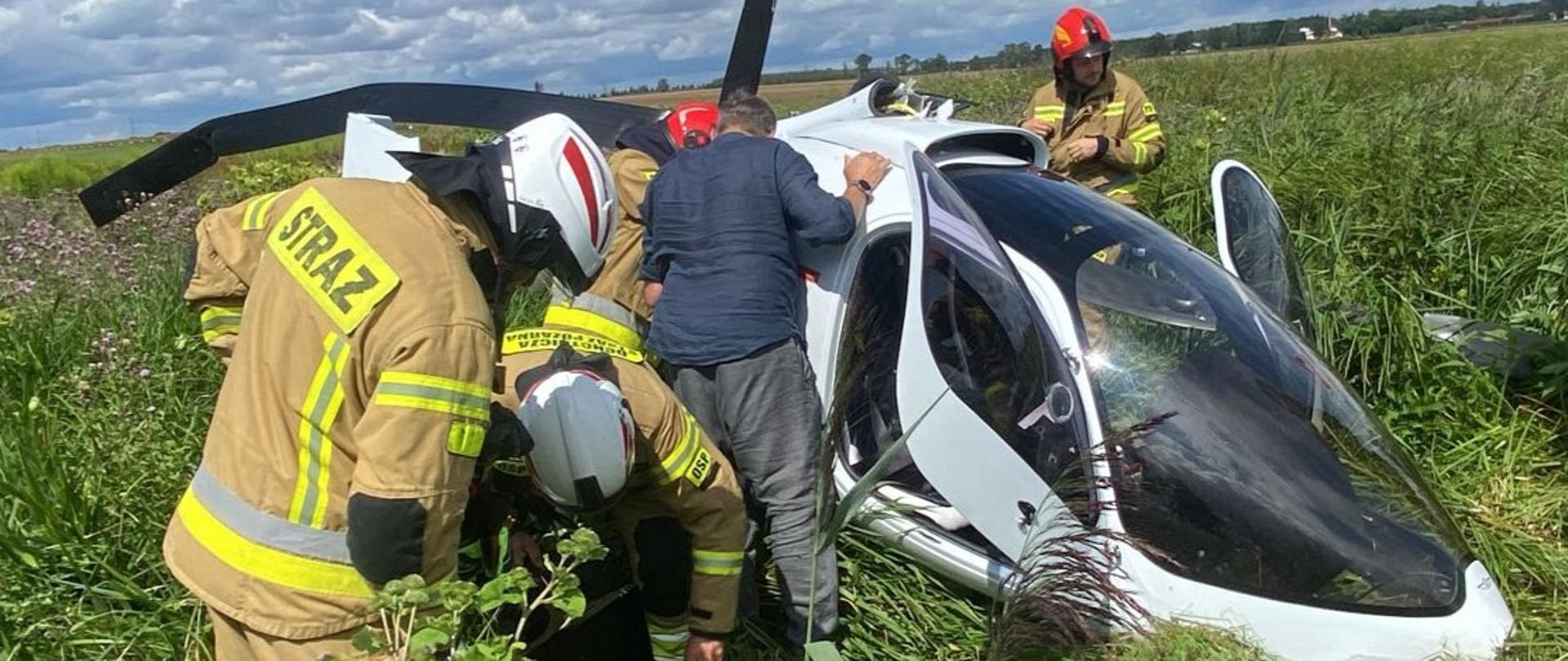 Uszkodzony wiatrakowiec na polu. Wokół strażacy działający na miejscu zdarzenia. 