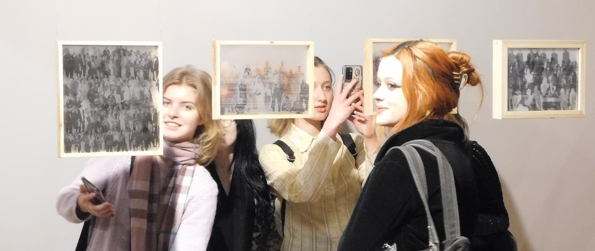 Cztery dziewczyny stojące z obu stron przestrzennie eksponowanych niewielkich serigrafii