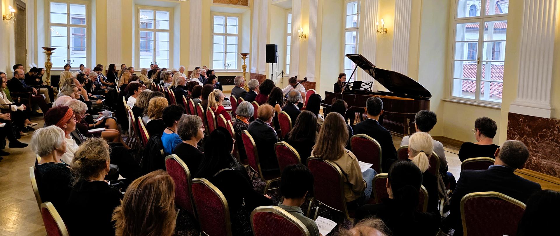 Pełna Sala Balowa Ambasady RP w Pradze. Przy fortepianie czeska pianistka Linda Juránková. Gra również polski wiolonczelista Fryderyk Midor.