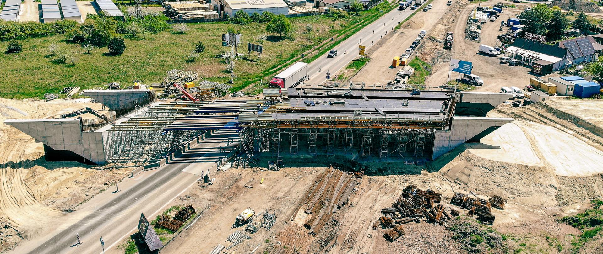 Na zdjęciu widoczne zabetonowane przyczółki oraz rozstawione rusztowanie i szalunki płyty głównej ustroju nośnego wiaduktu. Na placu budowy zgromadzono znaczne ilości stali zbrojeniowej.
