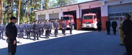 Na zdjęciu widoczni są strażacy podczas uroczystości rozpczęcia szkolenia podstawowego. W ich tle widoczne są dwa samochody ratowniczo-gaśnicze.
Po lewej stronie zdjęcia znajdują się kursanci, po prawej stronie zdjęcia przemawia Komendant Wojewódzki bryg. Grzegorz Słota.
