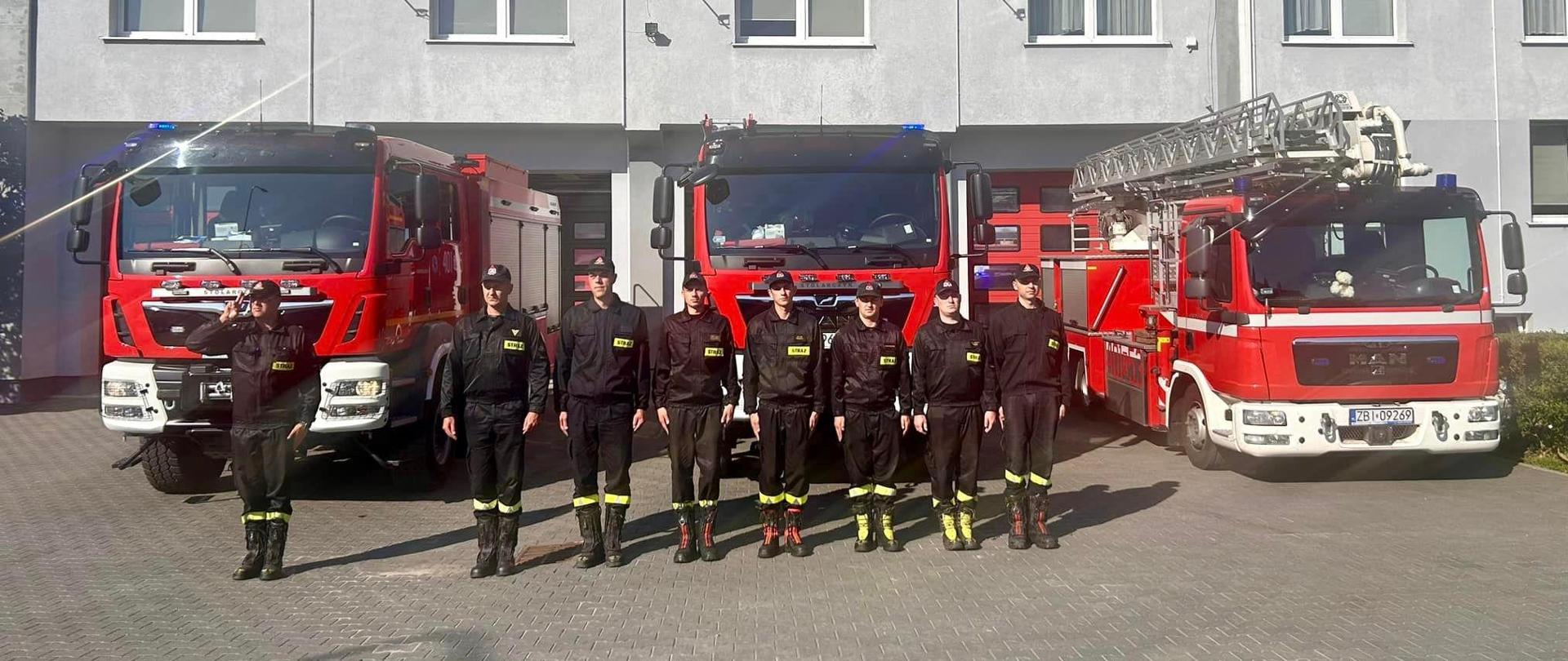 Zdjęcie wykonane przed budynkiem Komendy. W tle budynek, bliżej wozy strażackie a na pierwszym planie strażacy w szeregu.