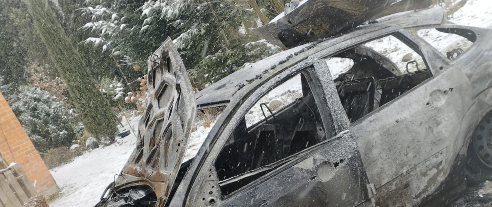 Na zdjęciu całkowicie spalony pojazd. Zdjęcie w ciągu dnia. Widać śnieg. W tle drzewa.