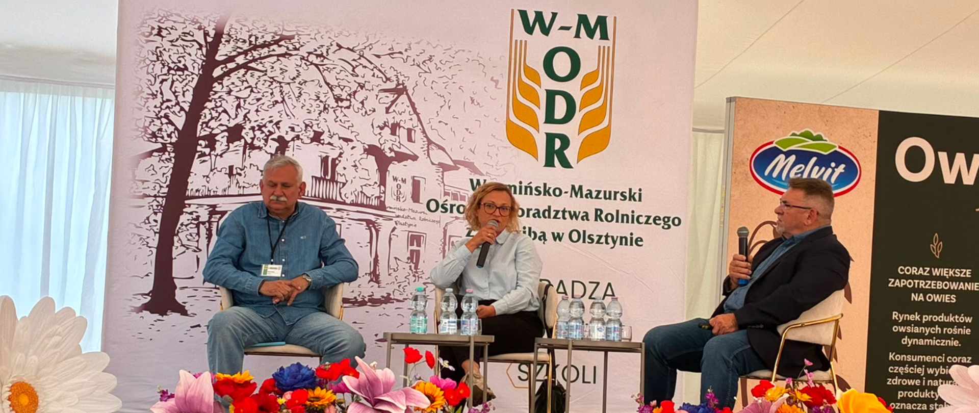 Trzy siedzące osoby. Pośrodku Zastępca Regionalnego Dyrektora Ochrony Środowiska - Regionalny Konserwator Przyrody w Olsztynie Aleksandra Krzysztoń-Rzodkiewicz przemawia przez mikrofon