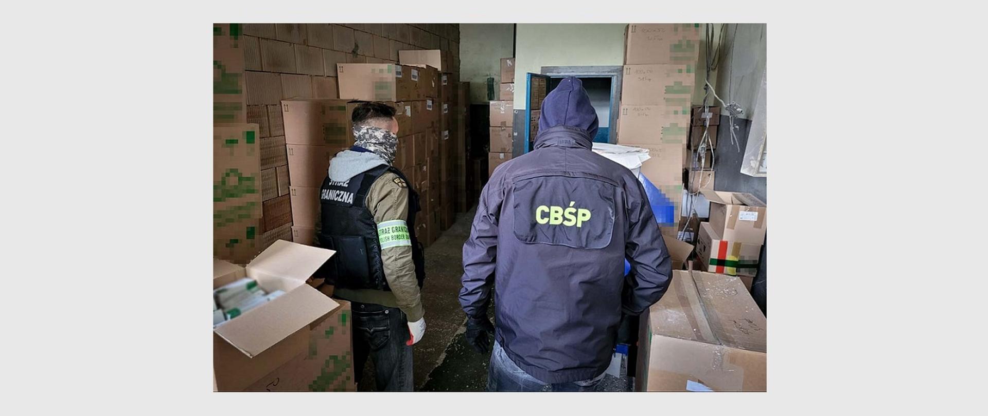 zdjęcie przedstawiające funkcjonariusza Straży Granicznej oraz funkcjonariusza CBŚP w pomieszczeniu, w którym znajdują się kartony 