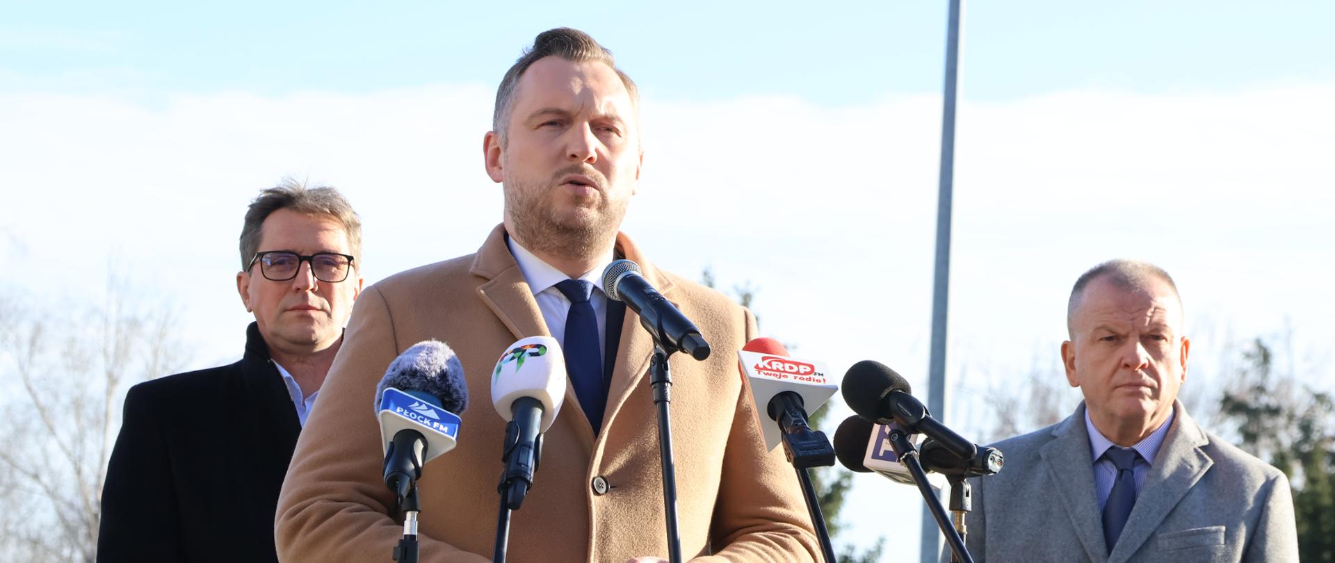 Podsekretarz Stanu w Ministerstwie Energii, Konrad Wojnarowski, przemawia przed mikrofonami na otwartej przestrzeni. Za nim stoją Sławomir Hinc, Prezes Zarządu GAZ-SYSTEM, oraz Robert Soszyński, Wiceprezes Zarządu ds. Operacyjnych ORLEN.