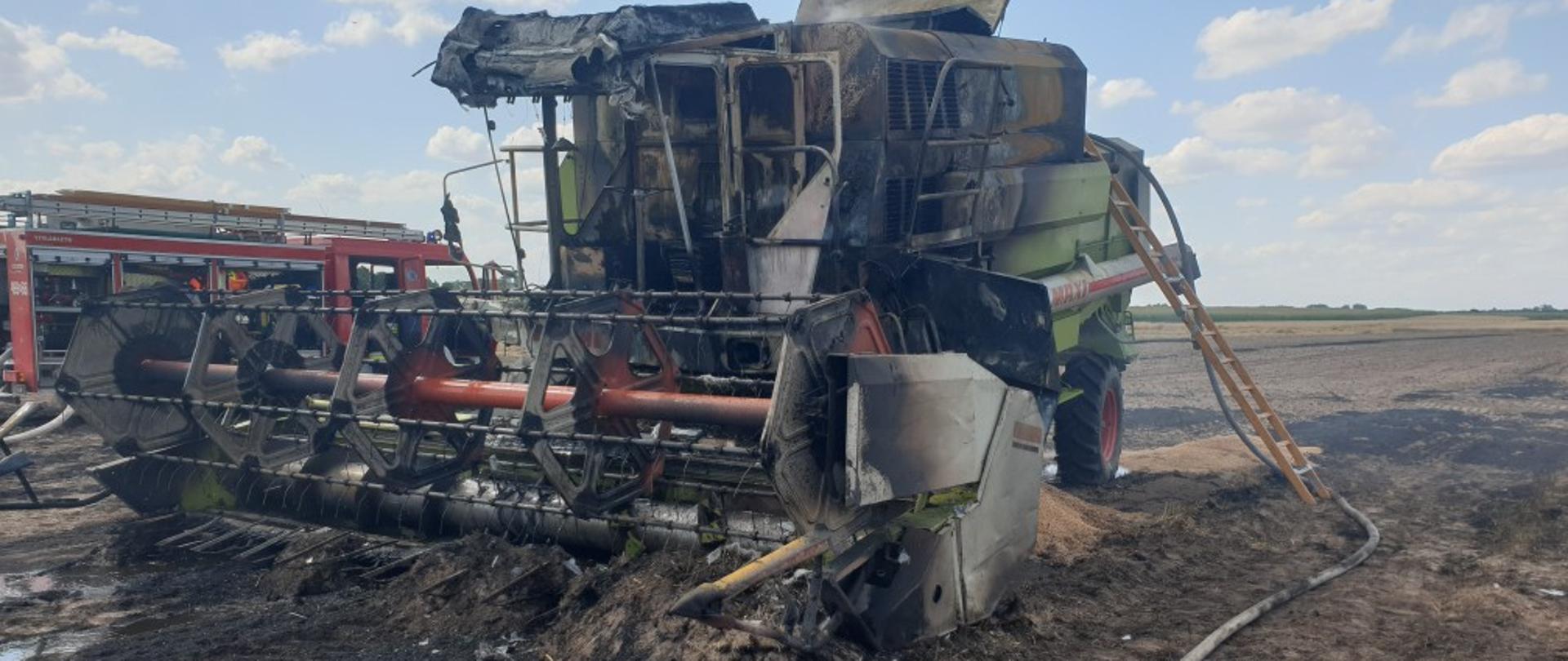 pożary podczas żniw. na zdjęciu widać stojący na polu spalony kombajn, w tle samochód pożarniczy i pola