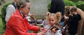 Dziewczynka próbująca grać na skrzypcach z pomocą nauczycielki