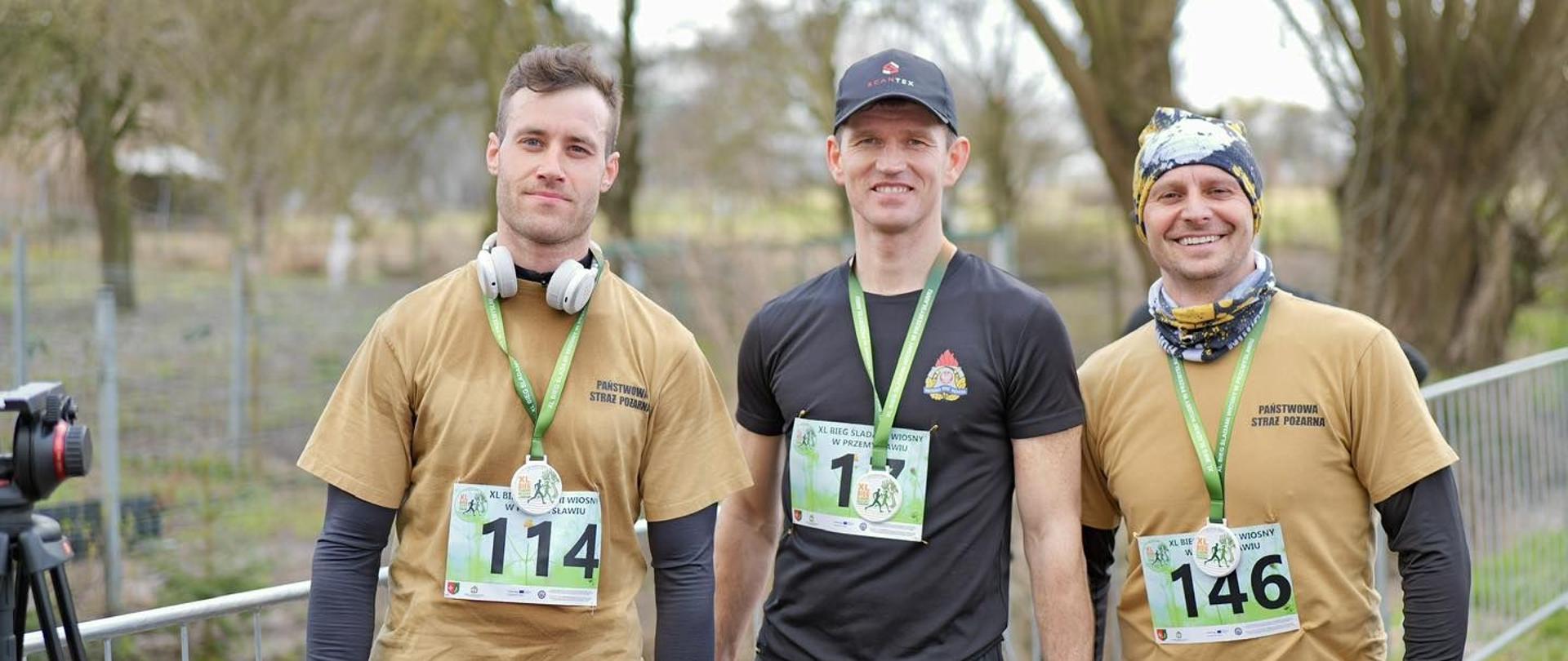Na zdjęciu trzech mężczyzn w strojach sportowych i z medalami na szyi. To braniewscy strażacy.