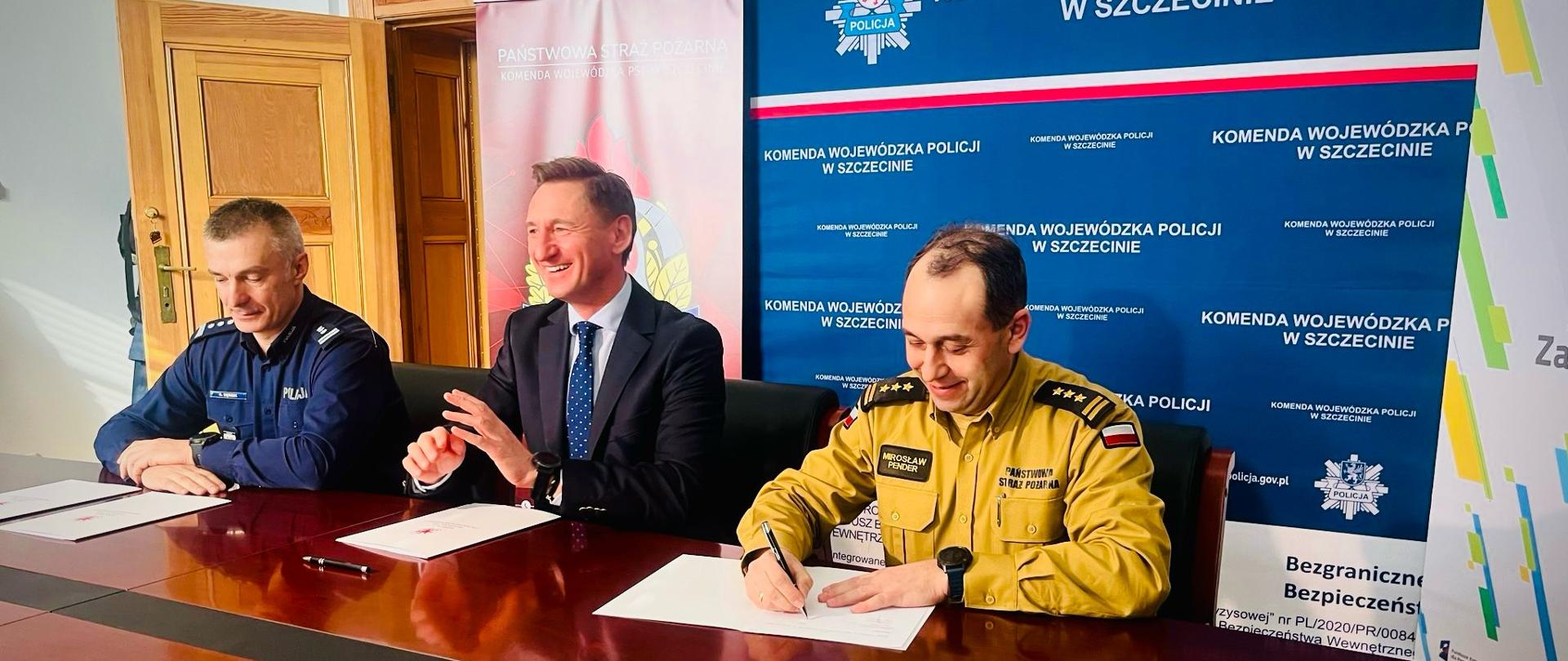 Patrząc od prawej, przy stole siedzi Zachodniopomorski Komendant Wojewódzki Państwowej Straży Pożarnej, Marszałek Województwa Zachodniopomorskiego i Zachodniopomorski Komendant Wojewódzki Policji. W tle widoczna jest niebieska ścianka medialna. Zdjęcie powiększy się po kliknięciu na nie.
