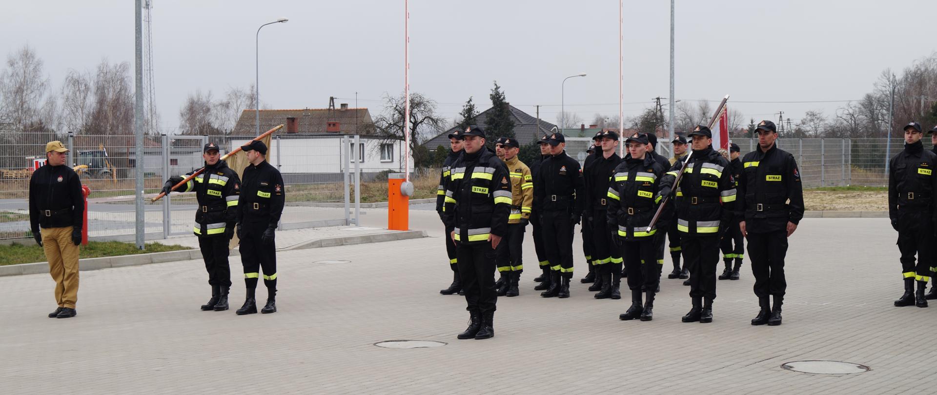 Zdjęcie przedstawia strażaków ze sztandarem ćwiczących musztrę