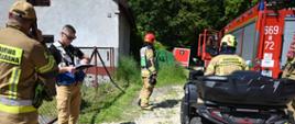 Kierujący działaniem ratowniczym odprawia strażaków przed włączeniem do działań, strażacy na quadzie i samochodach pożarniczych czekają na dyspozycje