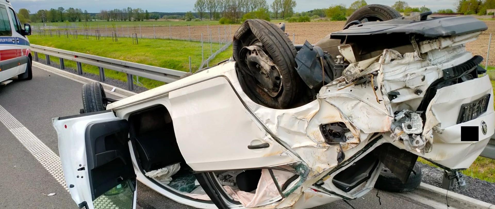 Mocno uszkodzony samochód osobowy leży na dachu na jezdni.