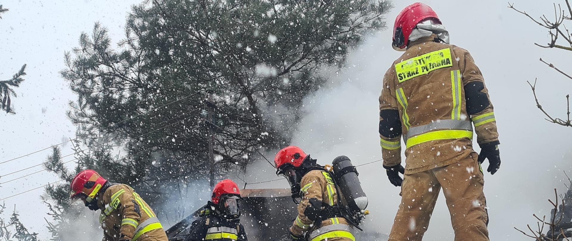Strażacy podczas działań gaśniczych stojący na dachu budynku, w tle wydobywający się z budynku dym
