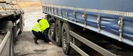 Inspektor świętokrzyskiej ITD kontroluje stan techniczny opon i układu hamulcowego naczepy ciężarowej.