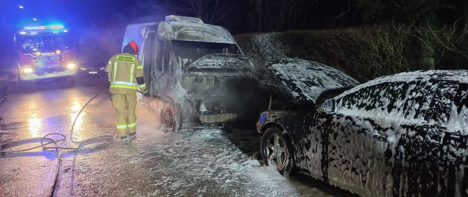 Zdjęcie przedstawia spalone dwa samochody osobowe oraz strażaka gaszącego je.